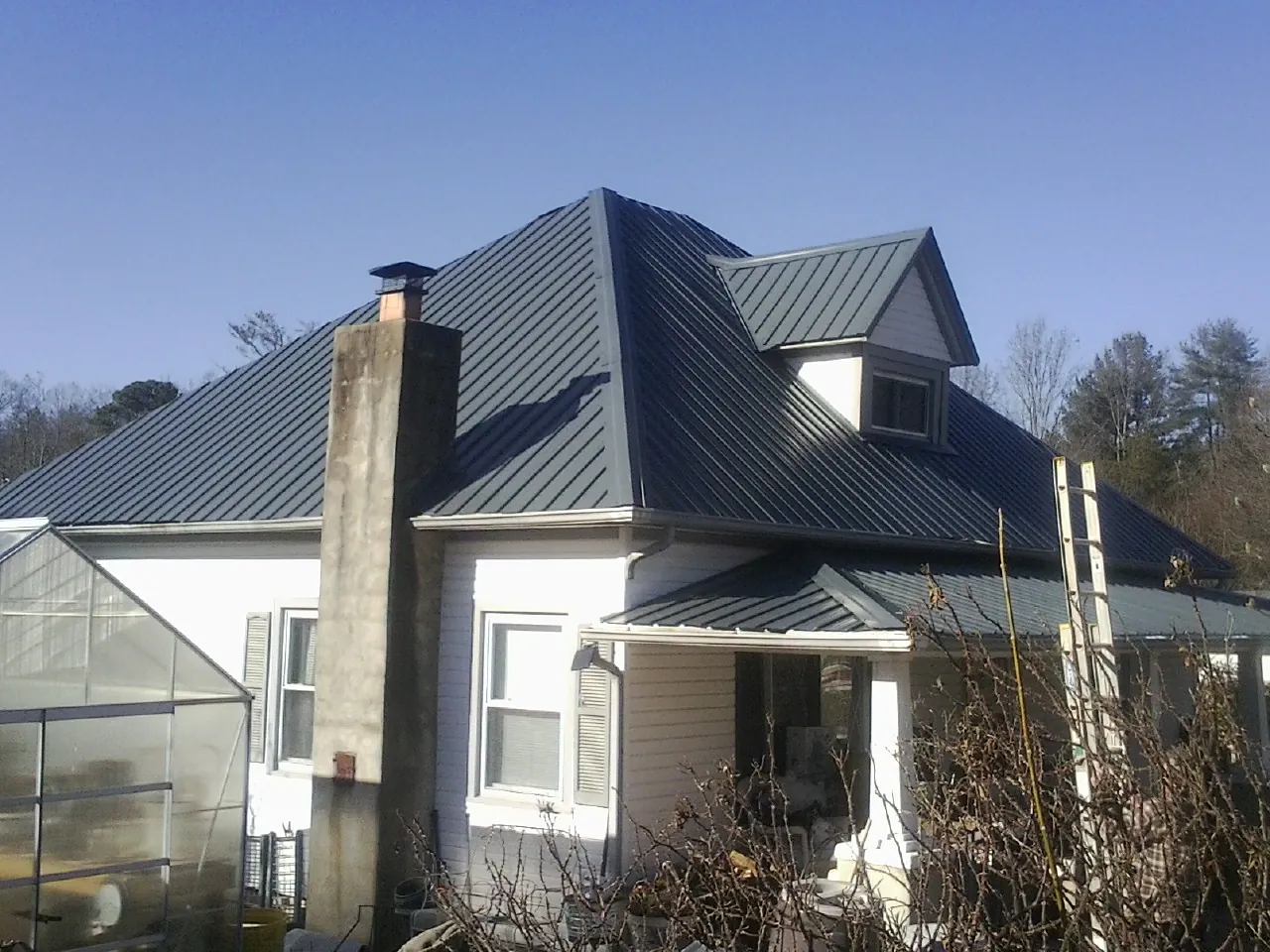 Dark blue standing seam metal roof on a white farmhouse with dormer — Slate & Tile Roof Repair by Roofing Brothers in Adolphus