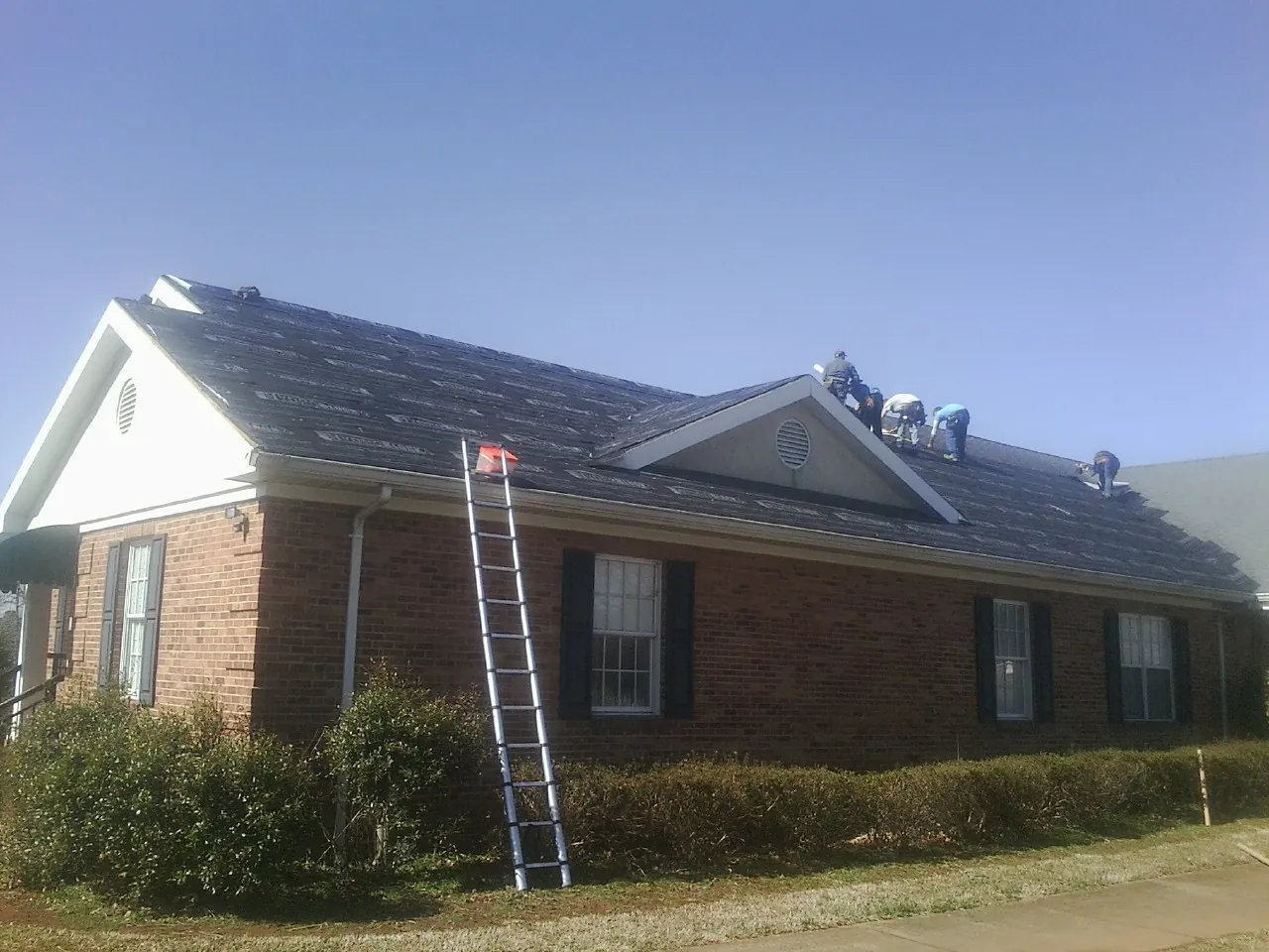 Crew tearing shingles off a brick ranch roof with a ladder set — Emergency Roof Repair work by our crew in Adolphus