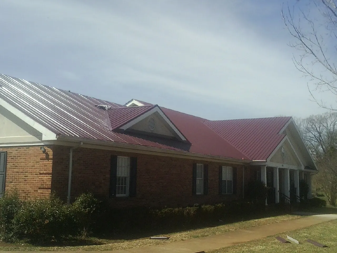 Red metal roof with gabled entries on a long brick building, from a Hail Damage Roof Repair job in Adolphus