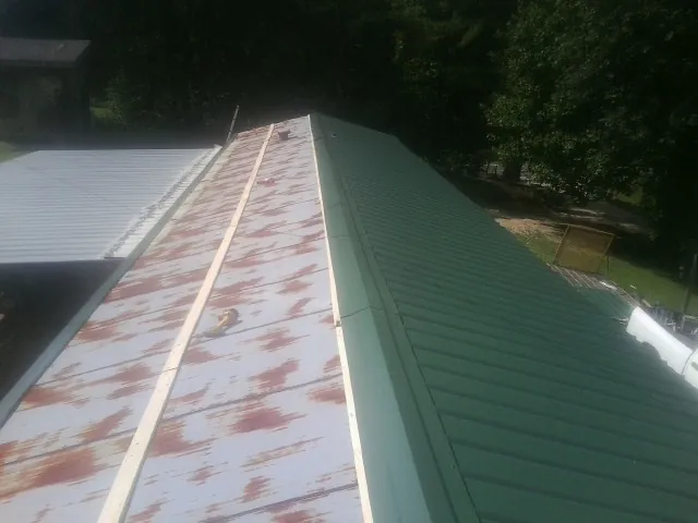 Old rusted panels beside newly installed green metal roofing — Wind Damage Roof Repair by Roofing Brothers in Adolphus