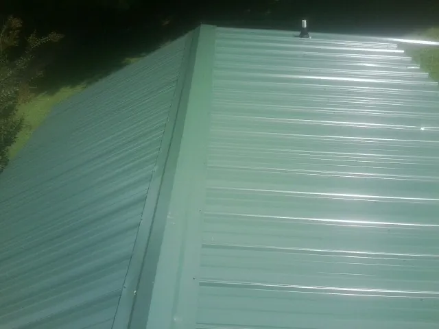 New green metal panels meeting at the ridge of a roof — Flat Roof Repair work by our crew in Adolphus