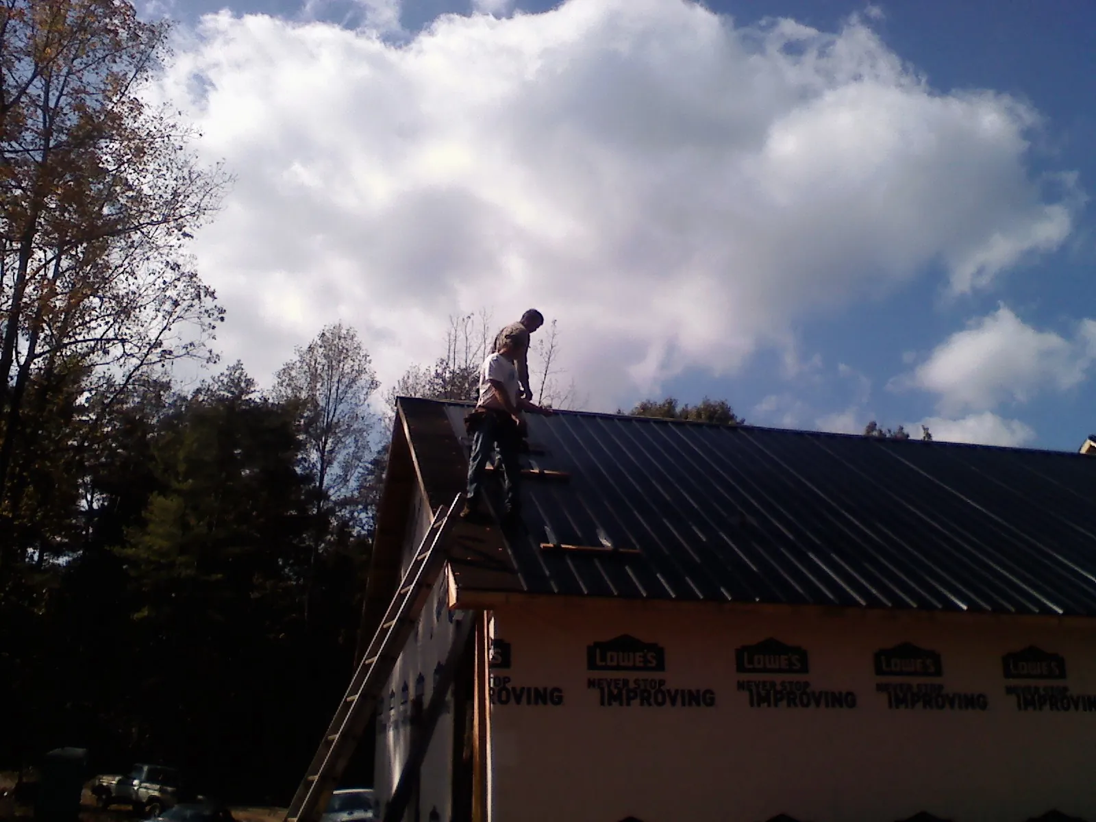 Roofer fastening dark metal panels high against a cloudy sky, from a Roof Inspection job in Adolphus