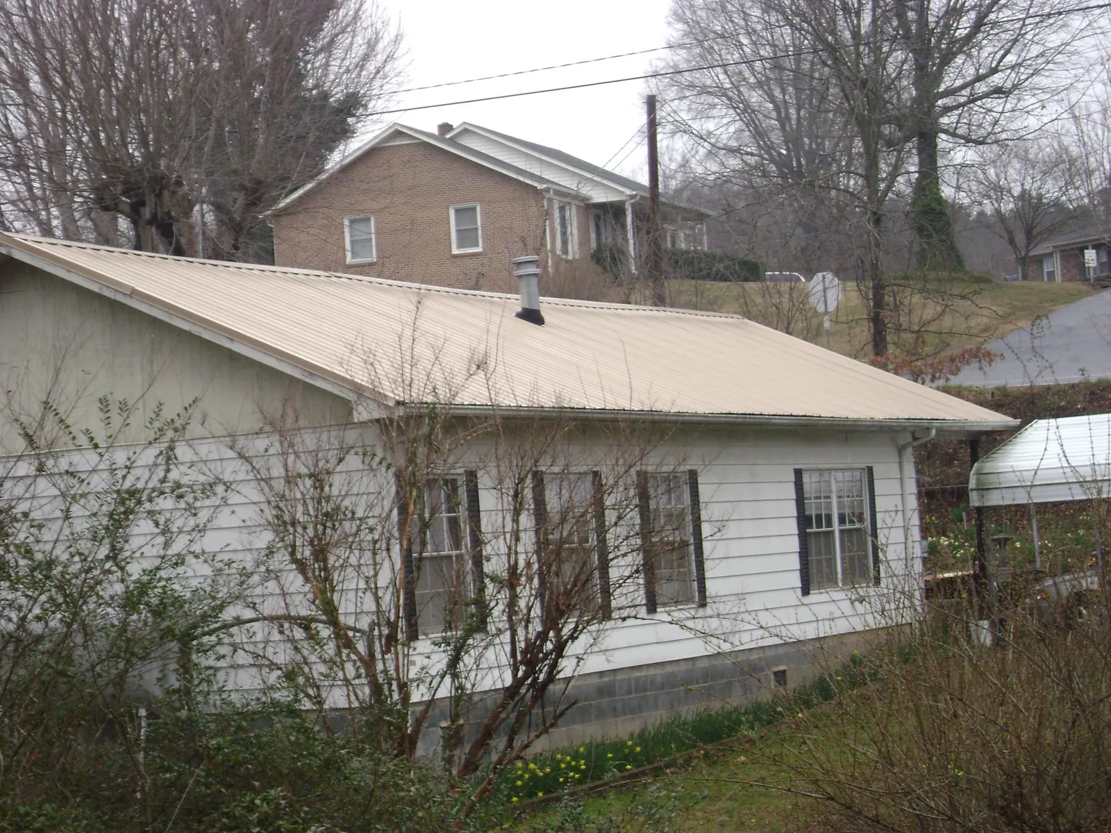 Tan metal roof on a white sided house set into a hillside — Commercial Roofing by Roofing Brothers in Adolphus